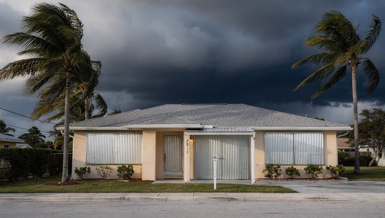 South Florida residential rental property with metal storm panels installed over windows under a darkening sky before a hurricane